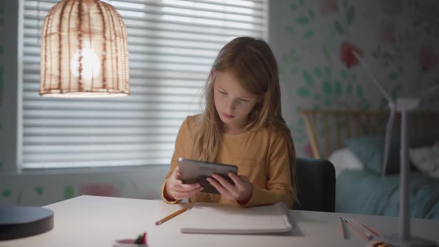 Girl using a tablet on a lit desk while studying