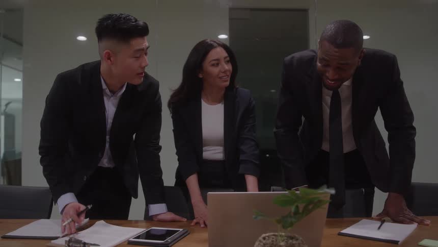 Three business professionals are engaged in a discussion around a laptop during a meeting