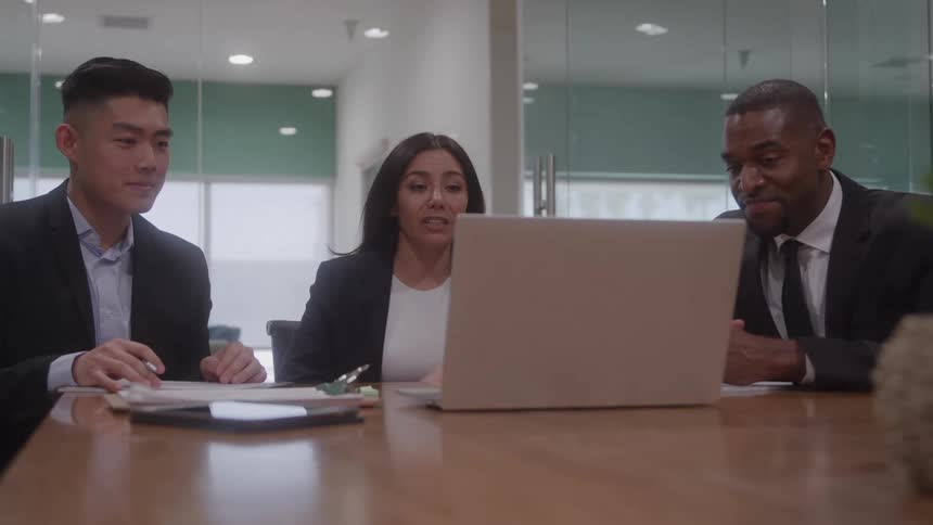 Three business people are gathered around a laptop for a video conference