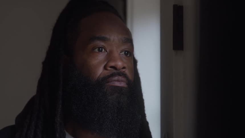 Man with a long beard looking thoughtfully out the window