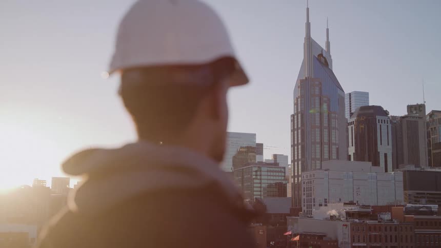Man wearing a hardhat stands looking at tall city buildings and skyscrapers