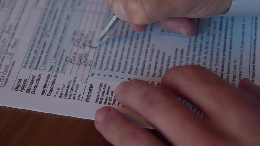 A persons hand is filling out a document with a pen on a wooden surface