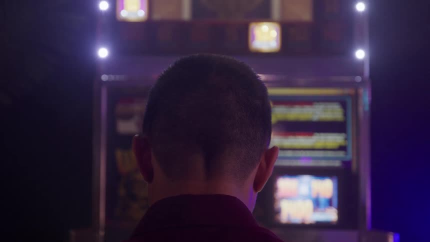 Lights flash on a machine as a man stands in an arcade