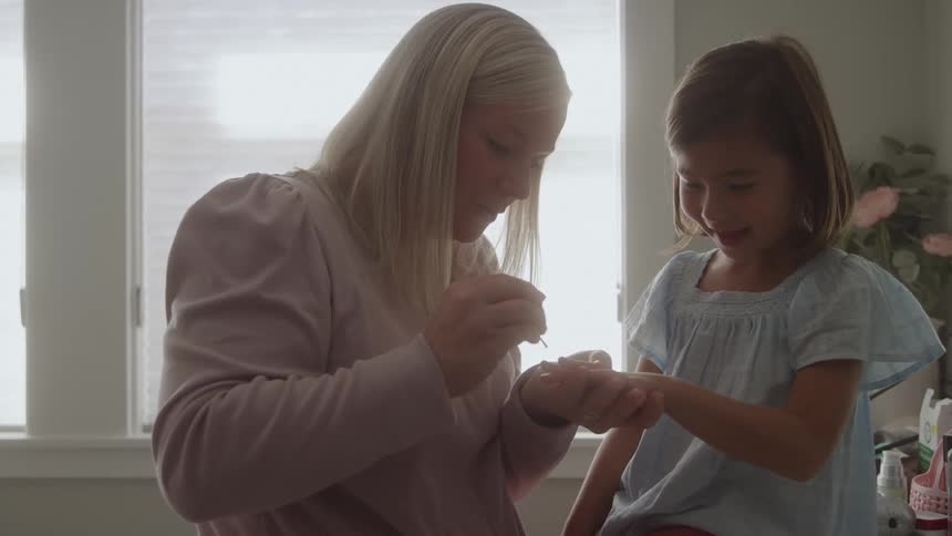 A woman is painting the nails of a smiling little girl in a well lit room