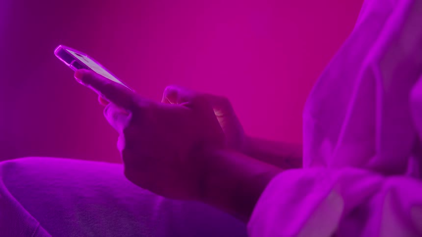 In a room bathed in vibrant pink and purple light a person texts on their smartphone