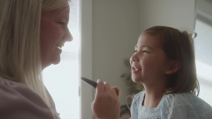 A mother brushes a childs face with a makeup brush