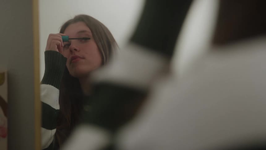 Young woman applying mascara to her eyelashes in front of a mirror