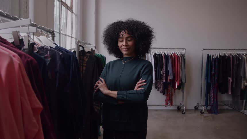 Woman standing with crossed arms among clothing racks in a fashion studio