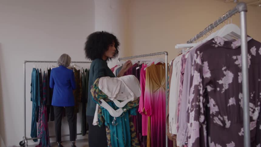 Two women inside a clothing store pick out clothes from the racks of dresses at midday