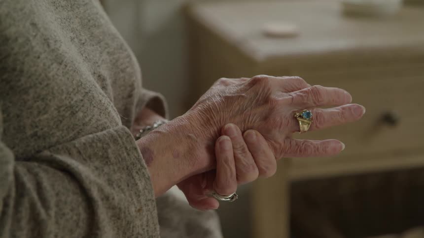 Elderly hands clasped with a slight gesture of pain or stiffness