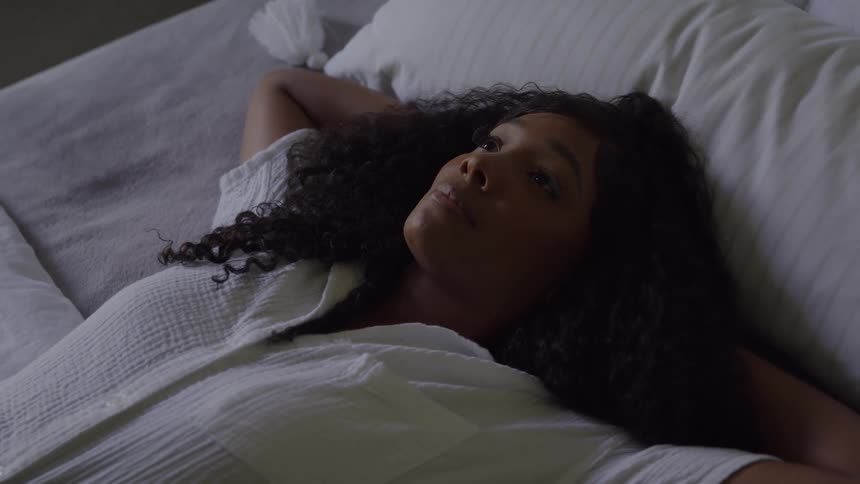 Woman lying on the bed with a thoughtful gaze toward the ceiling