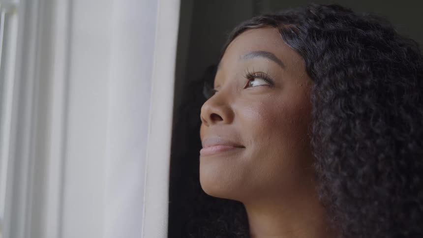 Woman smiles softly while looking out a bright window