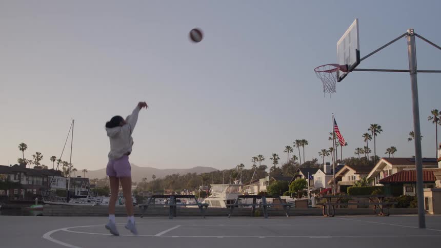 Teenage girl bounces the ball on the basketball court and throws it through the hoop