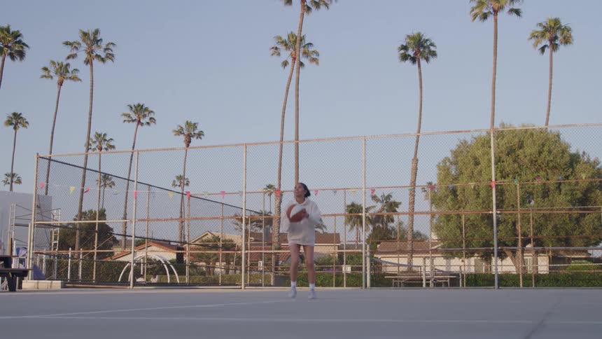 Person shooting a basketball on an outdoor court surrounded by palm trees