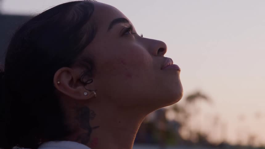 A woman with a neck tattoo looks up her face illuminated by the warm glow of sunset