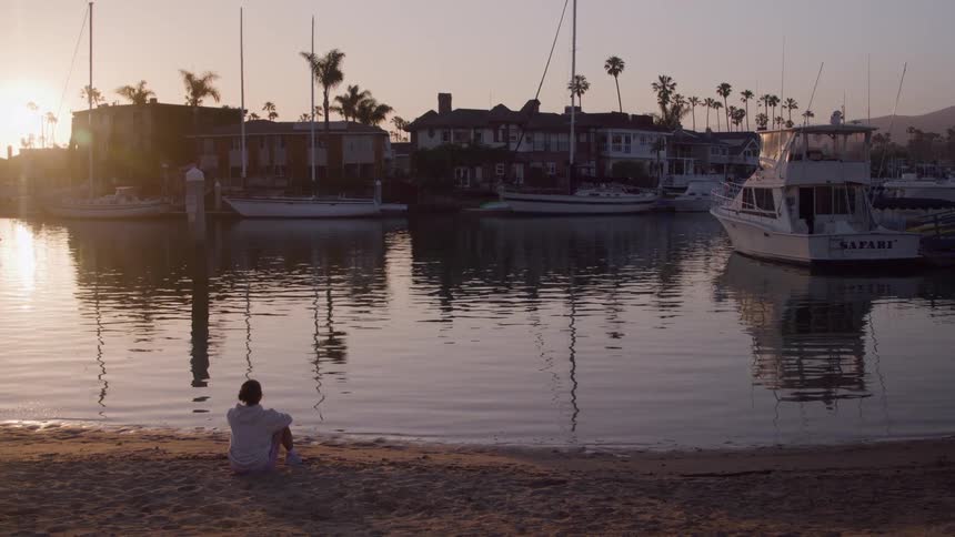 Coastal neighborhood with boats docked as a young man sits near the water