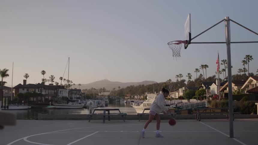 A young woman bouncing a basketball on the ground and then shooting it into a basketball hoop