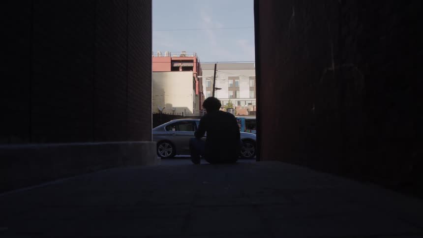 Young man sits on the stoop of a neighborhood building as traffic moves on the street
