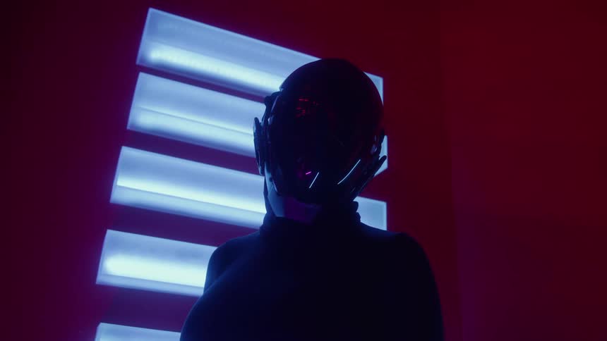 A person in a futuristic black helmet stands in a room illuminated by glowing blue lights