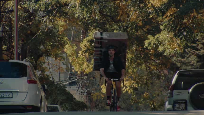 Male cyclist smiles while pedaling with a box strapped to his back on an autumn day