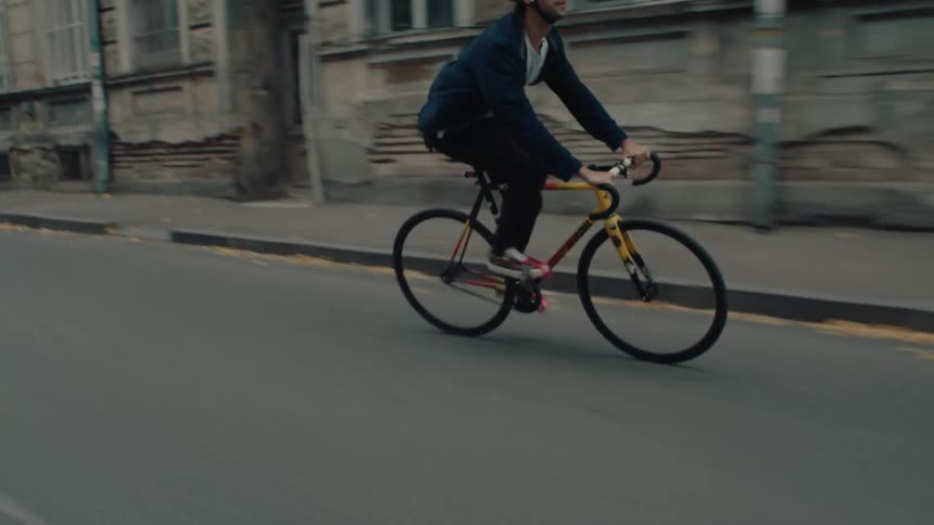 A man speeding down a city road on a bicycle zigzagging occasionally