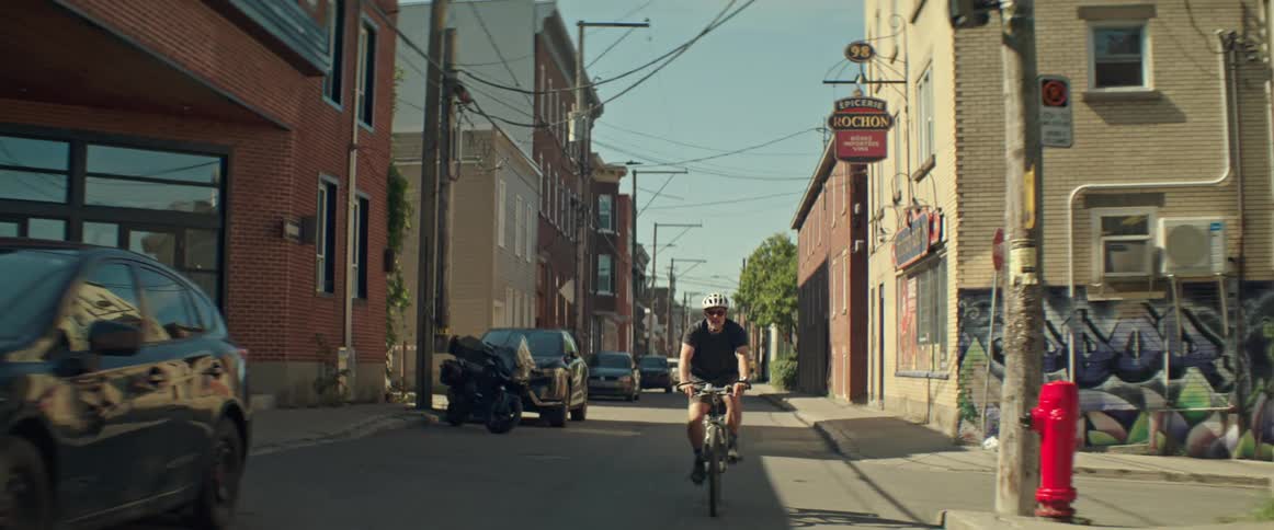 Man rides his bicycle on a neighborhood street between parked cars and buildings