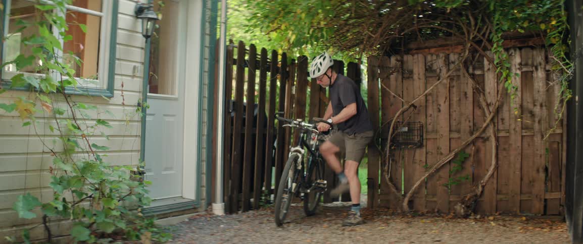 Male cyclist exits his backyard and cycles away on a summer day