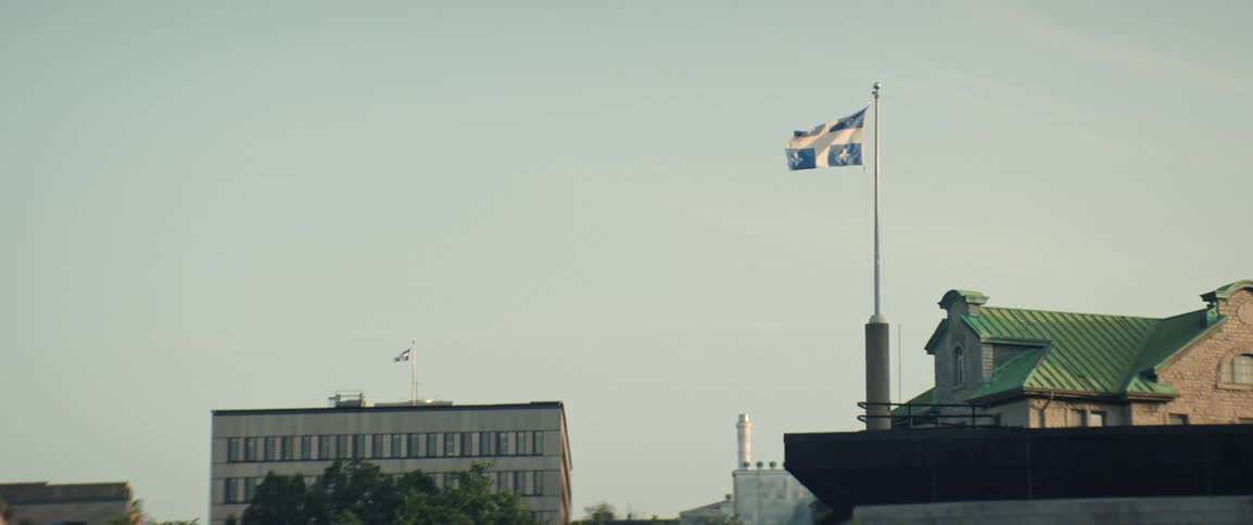 Quebec flag waves on a flagpole on the roof of a mid rise buildings on a summer day