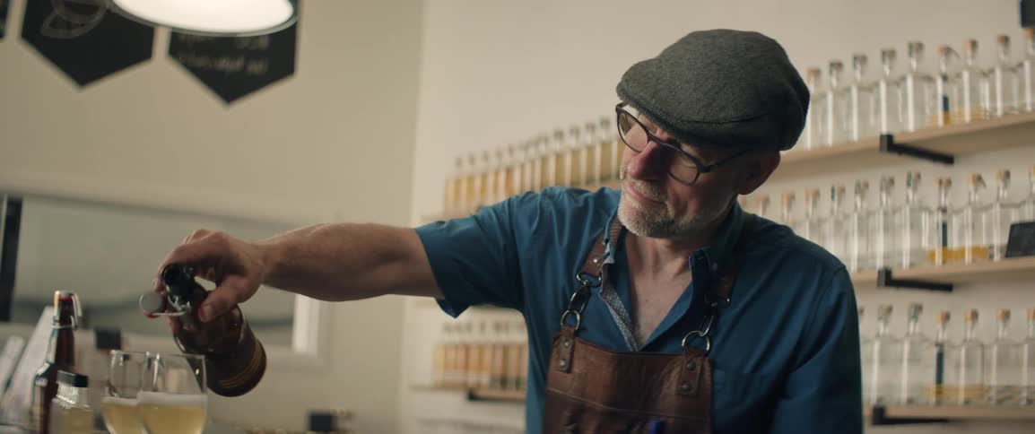 Man pours a golden drink into a glass inside a distillery