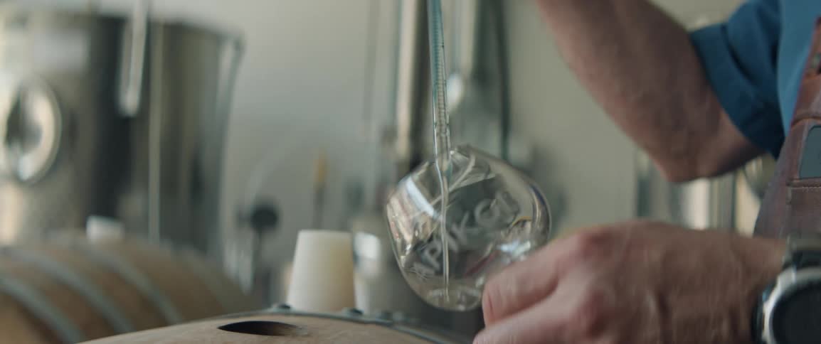 Hand holds a glass as a clear liquid is poured with a pipette