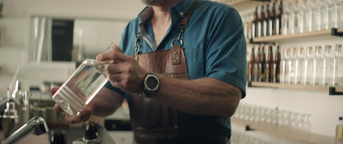 A man in an apron retrieves a bottle of liquor from a shelf