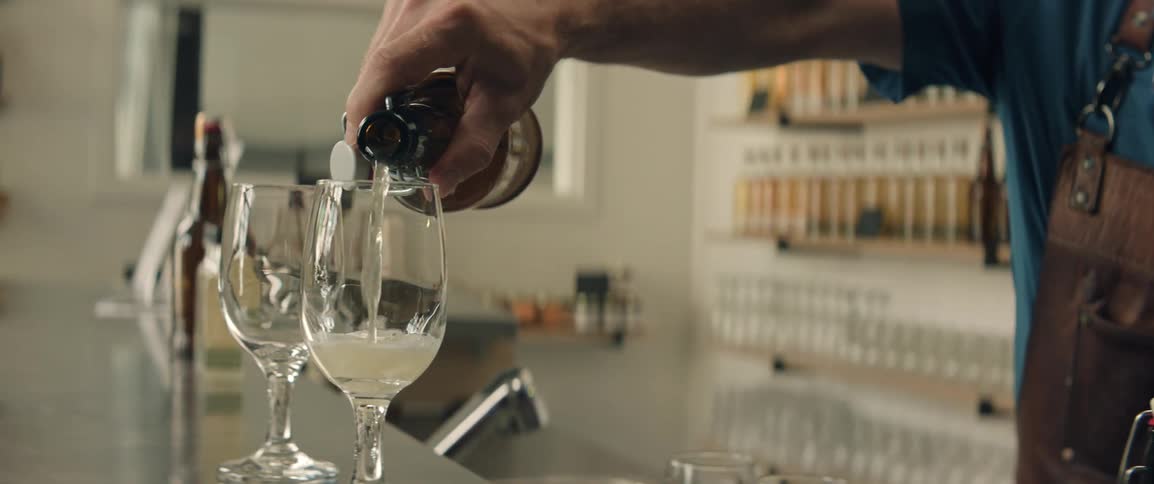 A man slowly pours a carbonated beverage into a glass goblet