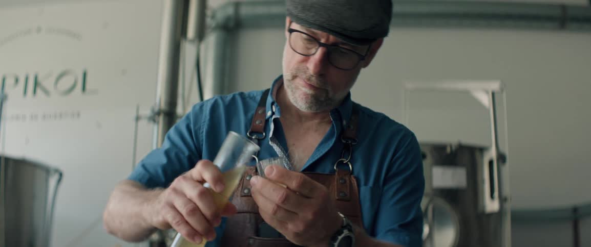 A man is working in a distillery and pours a liquid into a test tube