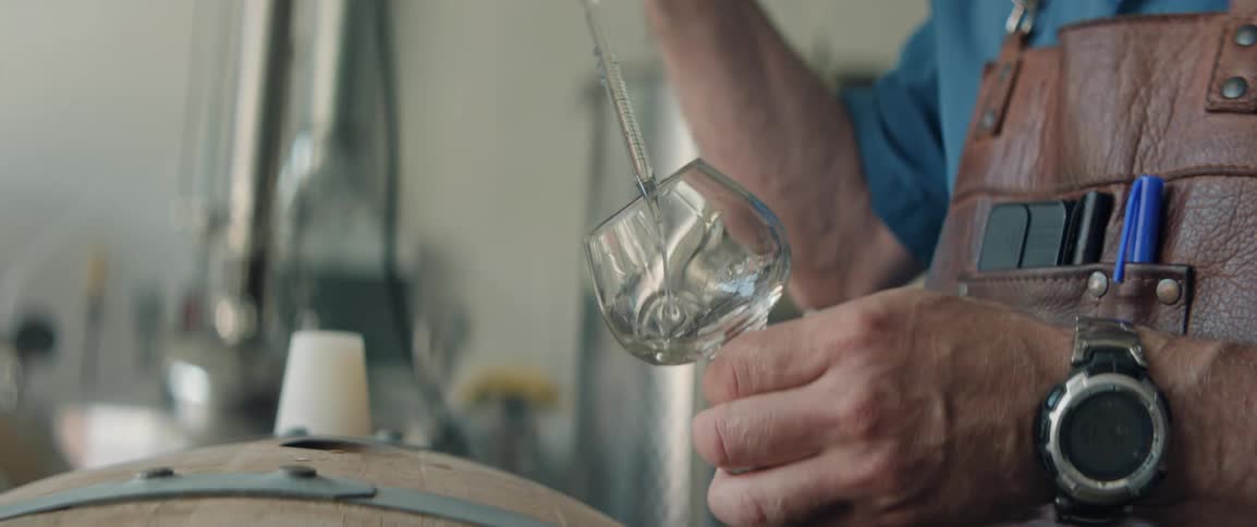 A man is taking a sample from a barrel and putting it in a glass