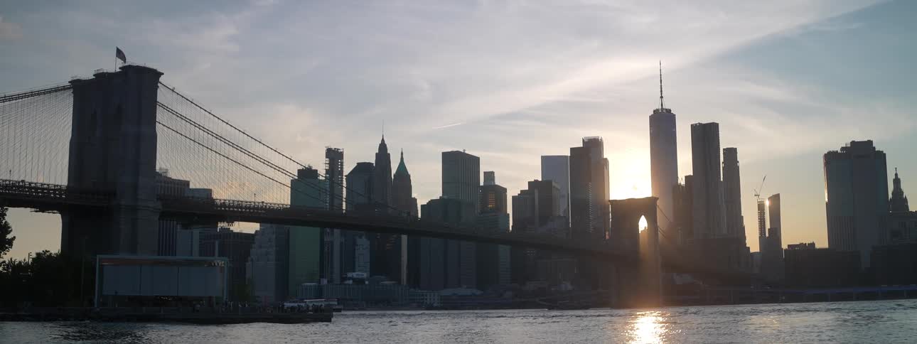 The brooklyn bridge crosses the east river to manhattan at sunset