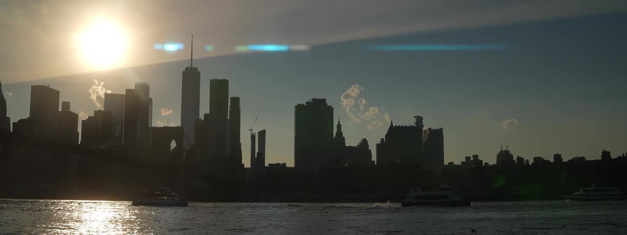 Boat sails near the bridge with the low sun lighting the urban skyline