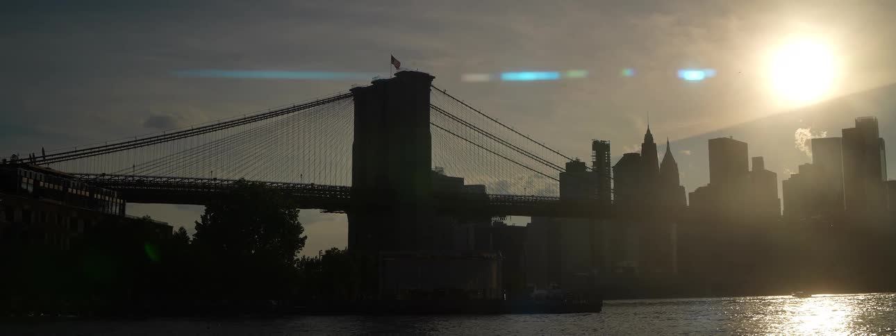 Suspension bridge silhouetted at sunset over the river and city