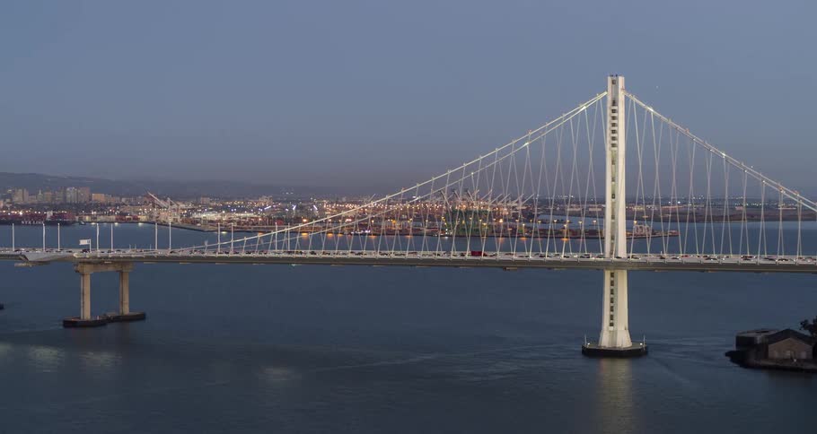 Aerial of a busy suspension bridge over a water body in a metropolitan area at sunset