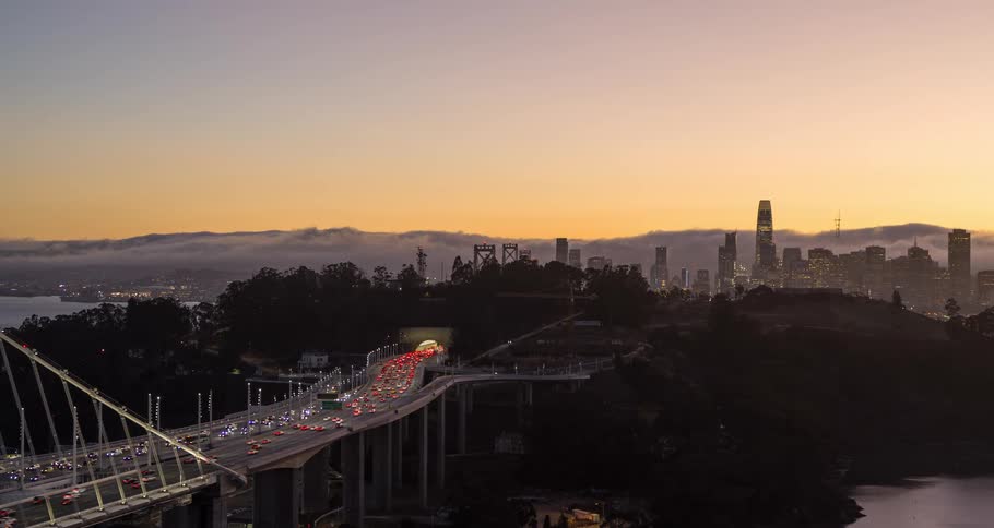 Traffic on the road and bridge into town with towers and skyscrapers on the city skyline and buildings along the coast