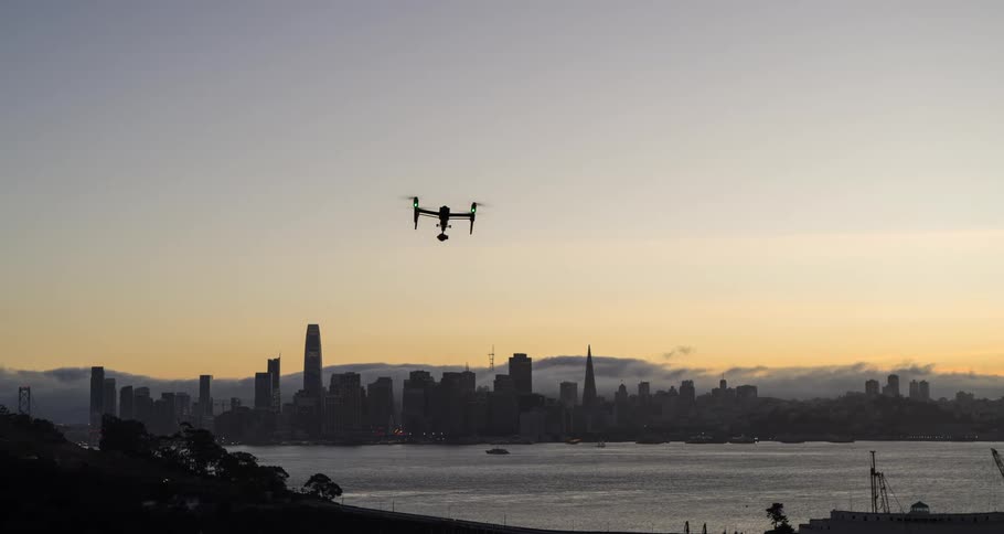 A drone hovering in a the air over a water body at sunset