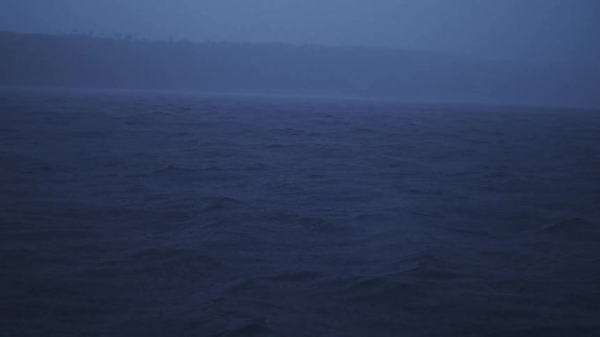 Dark choppy water moves under a hazy blue sky with a faint shoreline visible in the distance