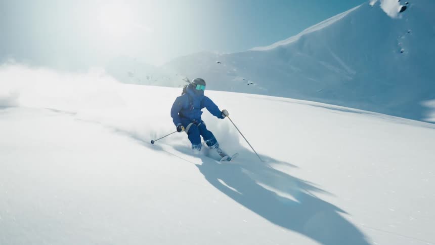 A skier in a blue jacket carves fast turns down a sunny mountain slope kicking up a spray of powder as the camera tracks their descent