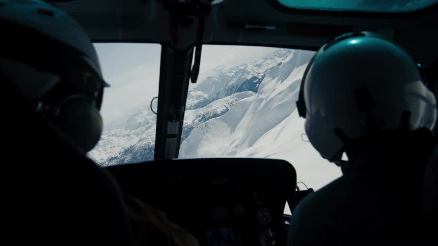View from inside a helicopter flying over snow covered mountains