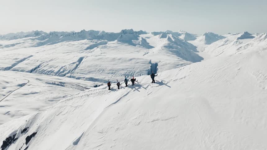 A group of hikers treks along a snowy mountain ridge amid towering white peaks