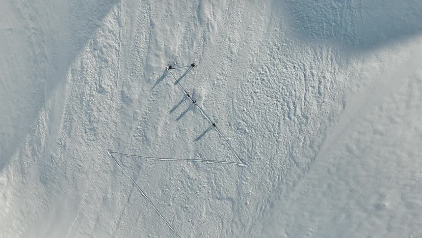 Aerial view of three people trekking across a snowcovered slope