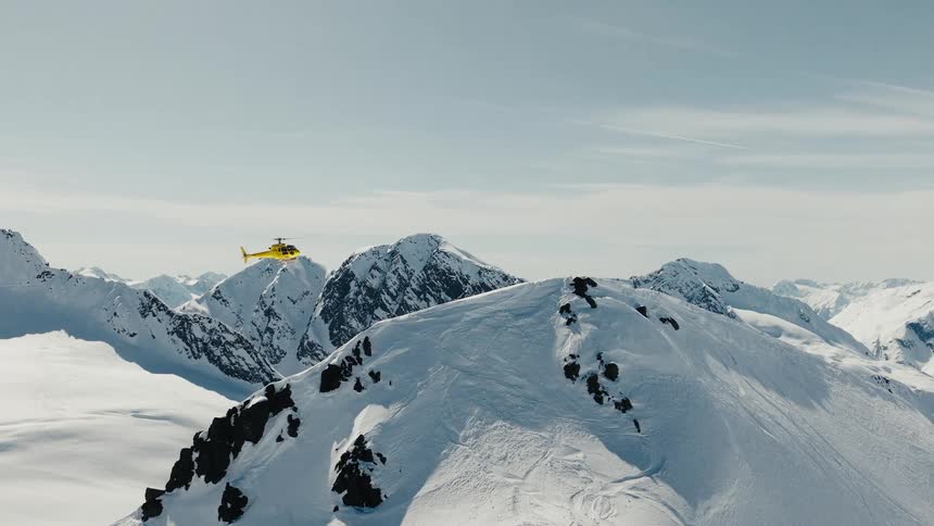 A helicopter flies over a snowcovered mountain during a winter midday
