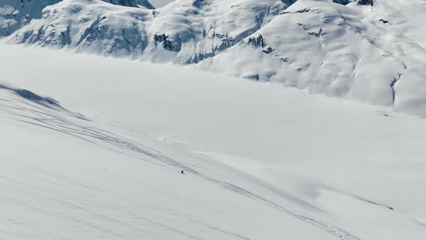 A skier carves fresh tracks down a pristine untouched mountainside
