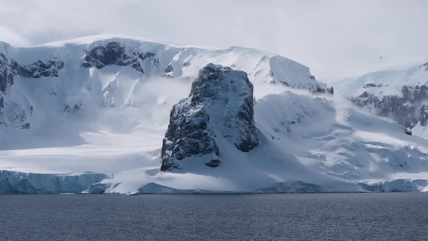 A snow covered rocky landscape is lined by ocean water