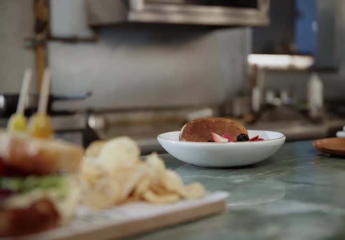 Chef plates a dessert while multiple chefs work in a commercial kitchen