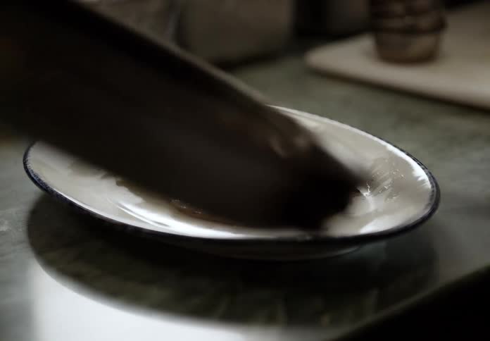 A persons hands are seen sliding eggs off a frying pan onto a plate with sausage on a countertop